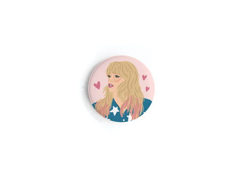Celebrate Taylor’s enchanting lyrics with the TS Lover Button Magnet by Onderkast Studio, featuring an illustrated blonde woman in a blue star-patterned outfit on a pink, heart-accented background.