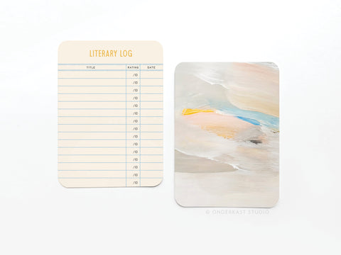 Two cards from the Onderkast Studio Literary Log Book Review Card Set are shown: one with columns for title, rating, and date, and another featuring an abstract pastel design on premium card stock.