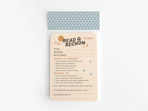 The Read & Reckon Book Review Card Set by Onderkast Studio includes beige, premium card stock cards with colorful prints. Each card features sections for title, author, date, and rating and comes in a clear bag with a blue star-patterned flap.