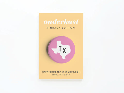 Show your Texas pride with the Pink TX Pinback Button from Onderkast Studio, featuring a white Texas outline and black Tx on a pink background. Attached to a yellow card with Onderkast PINBACK BUTTON and website info below.