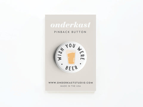 The Wish You Were Beer Pinback Button by Onderkast Studio showcases a vibrant beer glass print with WISH YOU WERE BEER—an ideal nostalgic gift for beer lovers, presented on an Onderkast Studio branded card.