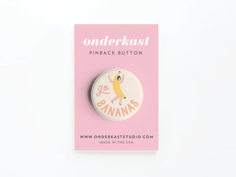 The Go Bananas Pinback Button by Onderkast Studio showcases a whimsical banana and go BANANAS text, packaged on a pink Onderkast pinback button card. Printed in the USA.