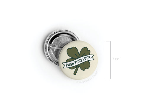 The Onderkast Studio Push Your Luck Clover Pinback Button is a 1.25 round button featuring a four-leaf clover and PUSH YOUR LUCK banner—a perfect Irish charm to add luck to your style.