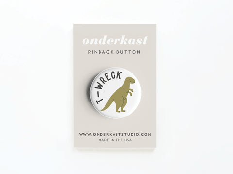 The discontinued T-wreck Pinback Button by Onderkast Studio features a cartoon T-rex and T-WRECK text on a vibrant round button, attached to a beige Onderkast Studio card with onderkaststudio.com.