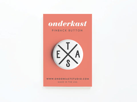 The Texas Logo Pinback Button by Onderkast Studio features TEXAS in an X shape, iconic imagery, and bold pride. Attached to a coral card reading onderkast PINBACK BUTTON. Includes website info and MADE IN THE USA.