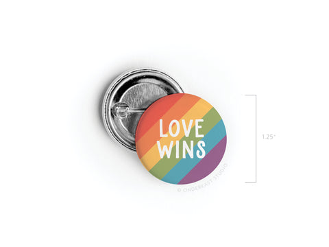 The 1.25-inch Love Wins Pinback Button by onderkast studio features diagonal rainbow stripes and bold white LOVE WINS text, shown front and back—ideal for LGBTQ+ allies and activists.