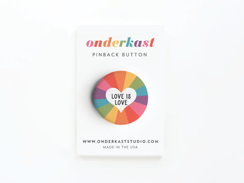 The Love Is Love Pinback Button by onderkast studio features a heart with LOVE IS LOVE at its center, displayed on a branded card. High-quality production. MADE IN THE USA printed at the bottom.