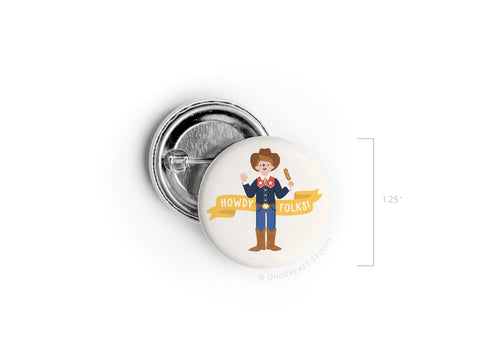 The Howdy Folks! Pinback Button by Onderkast Studio features a smiling cartoon cowboy with a lasso on a white background and yellow ribbon. Printed in the USA, this round button measures about 1.25 inches across.