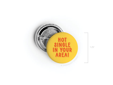 The Onderkast Studio Hot Single in Your Area! Pinback Button is round, yellow, and boldly says HOT SINGLE IN YOUR AREA! in red. Shown front and back, this 1.25-inch button features vibrant colors and a fun online dating joke design.