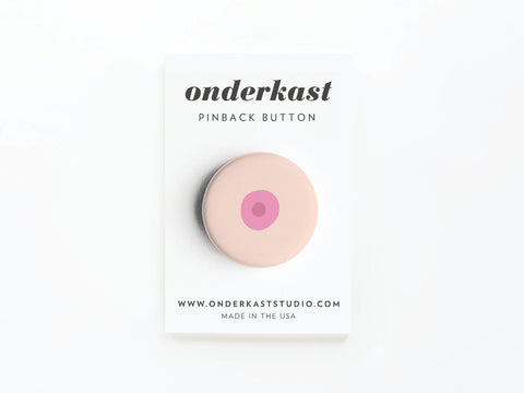 The Boob Pinback Button – Light by Onderkast Studio features a pink and dark pink breast-inspired circle design on a white backing card labeled onderkast PINBACK BUTTON, promoting self-love and body positivity. Made in the USA.