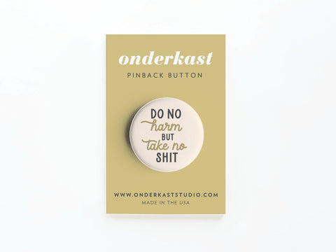 The Do No Harm But Take No Shit Pinback Button by Onderkast Studio features a bold design, attached to a tan card with studio info and Made in the USA details.