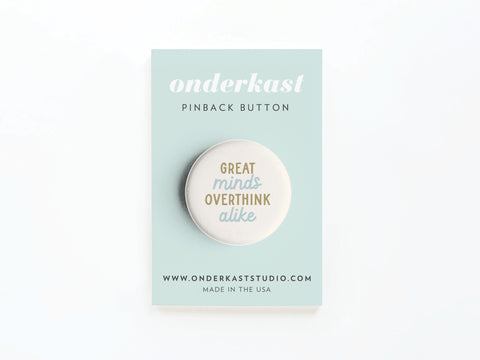 A round Great Minds Overthink Alike Pinback Button by Onderkast Studio, vibrantly printed and displayed on a light blue card featuring “onderkast pinback button,” “onderkaststudio.com,” and “Made in the USA.”.