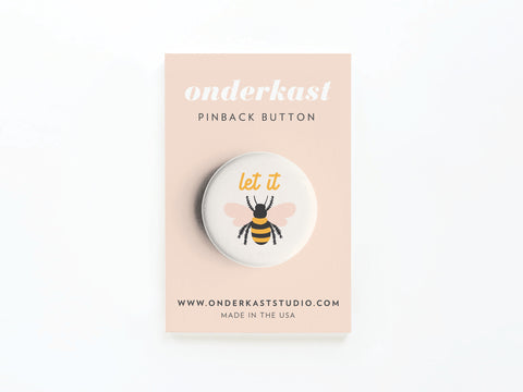 The Let It Bee Pinback Button by Onderkast Studio features a cartoon bee and “let it” in vibrant colors, comes carded, made in the USA—perfect for honeybee fans.