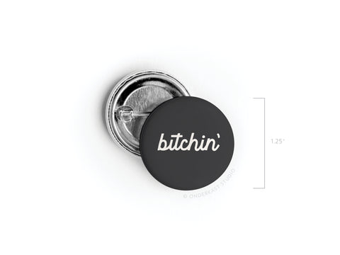 The Bitchin’ Pinback Button by Onderkast Studio features “bitchin’” in white cursive on a black background, measures 1.25 inches in diameter, and is made in the USA.
