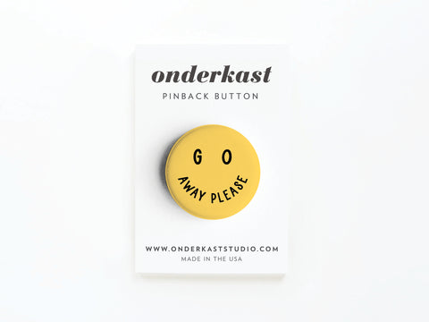 The Go Away Please Pinback Button by Onderkast Studio features a yellow smiley face and vibrant colors, attached to a white branded card—perfect for asserting personal space.