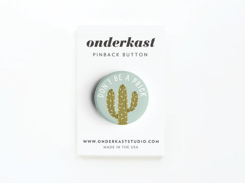The Don’t Be a Prick Pinback Button by Onderkast Studio features a cactus illustration and playful message, attached to a white branded card. Made in the USA. Learn more at www.onderkaststudio.com.