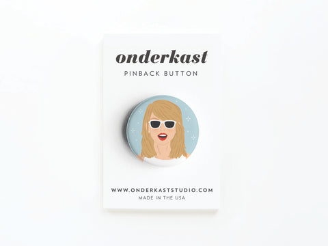 The Onderkast Studio TS 1989 Pinback Button features an illustrated woman with long blonde hair, white sunglasses, and red lipstick, attached to a branded card. Made in the USA and the website are printed at the bottom.