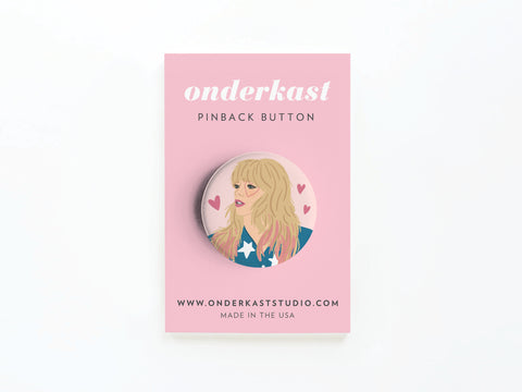 The TS Lover Pinback Button by Onderkast Studio features an illustrated woman and pink hearts on a round pin attached to a pink card labeled onderkast PINBACK BUTTON, with www.onderkaststudio.com and MADE IN THE USA printed on it.
