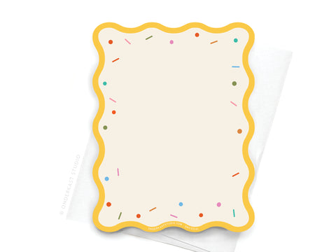 The Sprinkles and Wrinkles Wavy Die Cut Notecard by Onderkast Studio features a blank cream card with a wavy sprinkle border and colorful sprinkle accents, shown resting on a white napkin.