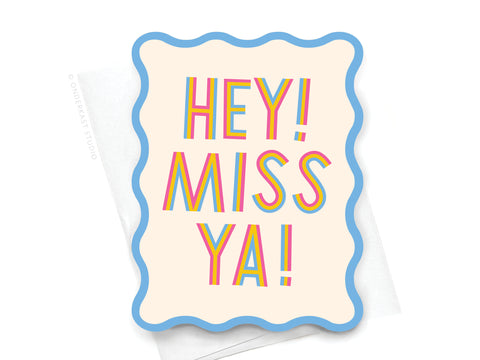 The Miss Ya Wavy Die Cut Notecard by Onderkast Studio features a colorful HEY! MISS YA! rainbow design on light beige with wavy blue edges, and comes with a white envelope.