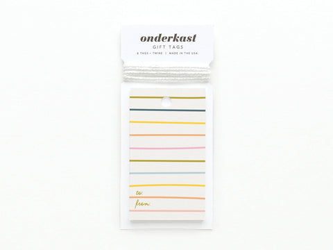 A pack of Onderkast Studio Bright Lines Gift Tags made from premium card stock, featuring vibrant horizontal stripes, a top hole for string, and gold “to:” and “from:” at the bottom. The header reads “Onderkast Gift Tags.”.