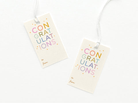 The Onderkast Studio Colorful Congratulations Gift Tag, printed in the USA, features playful CONGRATULATIONS letters with stars. Each card stock tag has “to:” and “from:” in cursive plus a white string attached. Set of two.