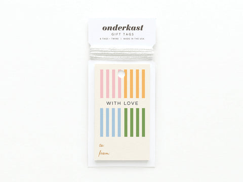 The With Love Cabana Stripes Gift Tag by Onderkast Studio is a hand-assembled white card stock tag with yellow, blue, pink, and green vertical stripes, WITH LOVE in the center, to/from at the bottom, and white string on top.