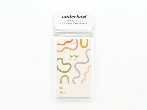 The Yay Squiggles Gift Tag by Onderkast Studio features abstract colorful squiggles and “yay!” on the front, with labeled spaces for to: and from:, all printed on premium card stock.