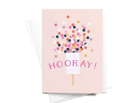 The Onderkast Studio Hooray! Confetti Popper Folded Greeting Note Set of 10 features vibrant colors and bold pink HOORAY! on a light pink card with a confetti popper design plus envelopes for a premium touch.