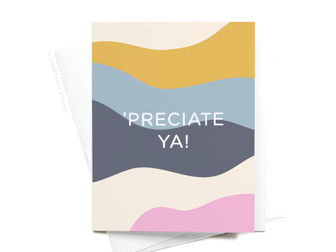 The ’Preciate Ya Greeting Card by Onderkast Studio features abstract wavy bands in mustard yellow, blue, dark gray, beige, and pink on cream with “PRECIATE YA!” in bold white letters. Printed in the USA.