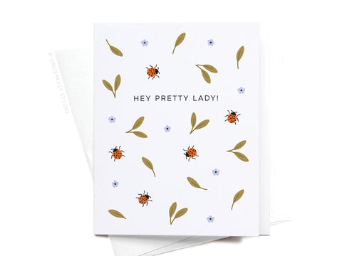 The Hey Pretty Lady Ladybugs Greeting Card by Onderkast Studio features vibrant ladybugs, green leaves, and blue flowers, with HEY PRETTY LADY! boldly centered on a white background for a premium touch.