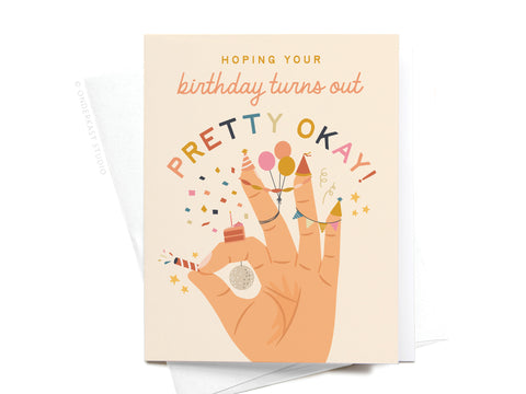 The Pretty Okay Birthday Greeting Card by Onderkast Studio features a hand with a party horn, confetti, cupcake, and colorful text: Hoping your birthday turns out pretty okay!.