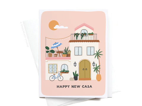 The Happy New Casa Greeting Card by Onderkast Studio shows a Spanish-style house with balconies, plants, a blue bicycle, and a sun. The card reads HAPPY NEW CASA at the bottom and comes with a white envelope.