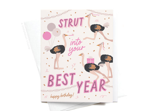 The Strut Into Your Best Year Ostrich Greeting Card by Onderkast Studio features illustrated ostriches, balloons, and a gift box with festive pink, gold, and white details. The card reads: Strut into your best year. Happy birthday!.
