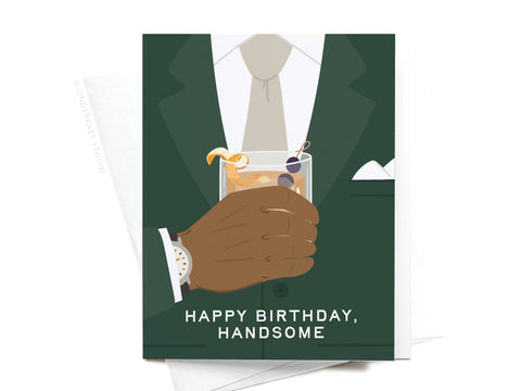 The Happy Birthday Handsome Greeting Card by Onderkast Studio features a man in a dark suit holding a cocktail with an orange twist and cherry, set against a dark background. The card reads “HAPPY BIRTHDAY, HANDSOME” at the bottom.