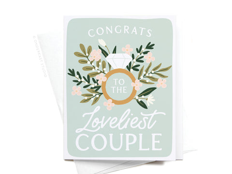 The “Congrats to the Loveliest Couple Greeting Card” by Onderkast Studio features floral art and a diamond ring, with white and gold lettering on light green. Printed in the USA.