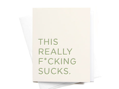 The Onderkast Studio This Really F*cking Sucks Letterpress Greeting Card features pale green text on white card stock and comes with a matching white envelope.