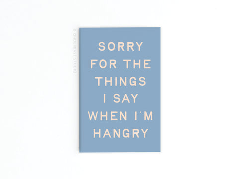 The Hangry Refrigerator Magnet by Onderkast Studio features beige text on blue, humorously saying Sorry for the things I say when I’m hangry, displayed with vibrant colors on a white background.