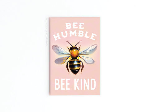 The Onderkast Studio Bee Humble Bee Kind Refrigerator Magnet is pastel pink with a central bee illustration and white text that reads “BEE HUMBLE” above and “BEE KIND” below.
