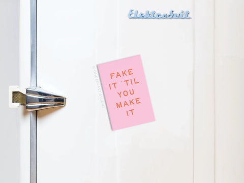 A pink Fake It ’Til You Make It Refrigerator Magnet by Onderkast Studio with orange text is displayed on a white fridge featuring a silver handle, blue Elektrobit logo, and “Made in USA” mark.