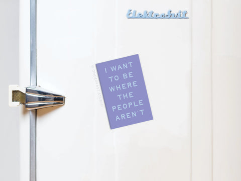 A white fridge with a silver handle sports Onderkast Studio’s “Be Where the People Aren’t” magnet, featuring introverted humor. The product name appears in blue at the top right.