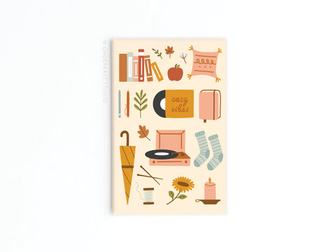 The Cozy Vibes Refrigerator Magnet by Onderkast Studio features autumn-inspired designs like books and a record player, printed in vibrant colors and warm, earthy tones to bring relaxation and cozy charm to your space.