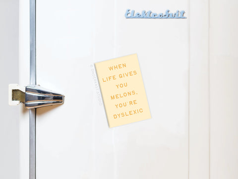 A vibrant yellow sticky note on a white fridge reads, WHEN LIFE GIVES YOU MELONS, YOURE DYSLEXIC. Its held by the Onderkast Studio Life Gives You Melons Refrigerator Magnet just below the brand name.
