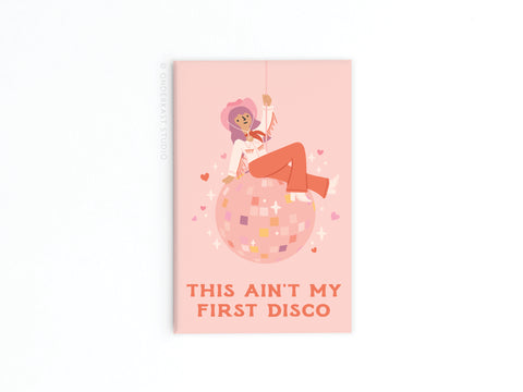The Ain’t My First Disco Refrigerator Magnet by Onderkast Studio features a pink, vibrant design of a smiling person in a cowboy hat and boots on a disco ball, with hearts and sparkles, plus the bold text: THIS AINT MY FIRST DISCO.