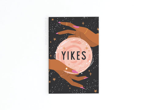 The Yikes Fortune Teller Refrigerator Magnet by Onderkast Studio showcases two hands with long pink nails holding a glowing YIKES crystal ball against a starry background.