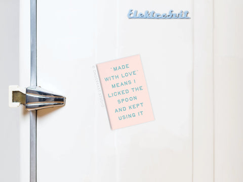 The Licked the Spoon Refrigerator Magnet by Onderkast Studio features a vibrant design and holds a pink note: “Made with love means I licked the spoon and kept using it.” Ideal for adding charm to any baking space.