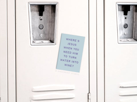 A note on a white locker reads, WHERES JESUS WHEN YOU NEED HIM TO TURN WATER INTO WINE? The Onderkast Studio Water Into Wine Refrigerator Magnet shows this phrase in vibrant colors and is centered between two locker doors.