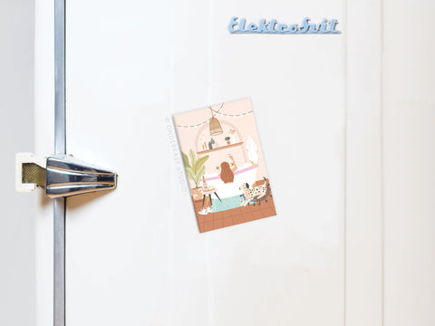 A postcard showing a person reading on a bed is attached to a white vintage fridge with a metal handle and the Bubblebath Cheers Refrigerator Magnet by Onderkast Studio—a charming accent for any self-care routine.