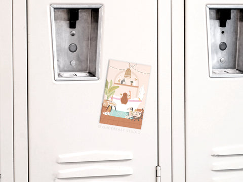A white locker features the Bubblebath Cheers Refrigerator Magnet by Onderkast Studio, showing a girl enjoying self-care with her cat, plants, and cozy decor in her room.