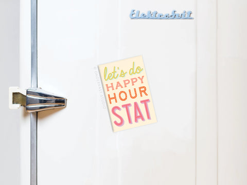 A white fridge displays the Happy Hour Stat Refrigerator Magnet by Onderkast Studio, featuring the phrase “let’s do HAPPY HOUR STAT” in bright colors—perfect fun kitchen decor with Elektrobit in light blue at the top right.